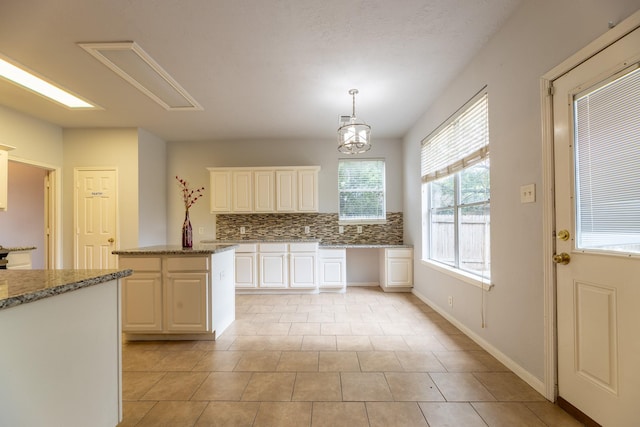 kitchen with decorative backsplash, light stone countertops, white cabinetry, light tile patterned floors, and decorative light fixtures