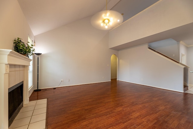 unfurnished living room with arched walkways, a fireplace, wood finished floors, baseboards, and high vaulted ceiling