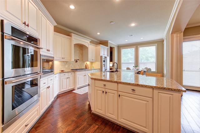 kitchen with appliances with stainless steel finishes, a sink, an island with sink, tasteful backsplash, and ornamental molding