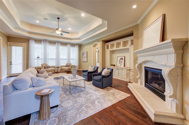 living area featuring ceiling fan, crown molding, arched walkways, a high end fireplace, and dark wood-style floors