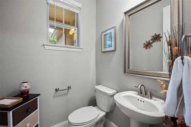 half bath with baseboards, toilet, and a sink