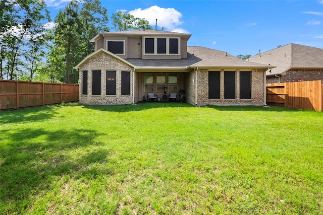 back of house featuring a lawn, roof with shingles, brick siding, and a fenced backyard