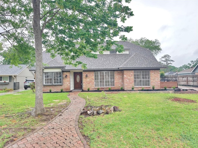 view of front facade featuring brick siding, fence, a front yard, and roof with shingles