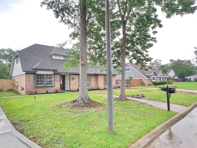 view of front of property with a front yard, roof with shingles, fence, and brick siding