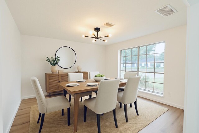 dining area with light wood finished floors, visible vents, a chandelier, and baseboards