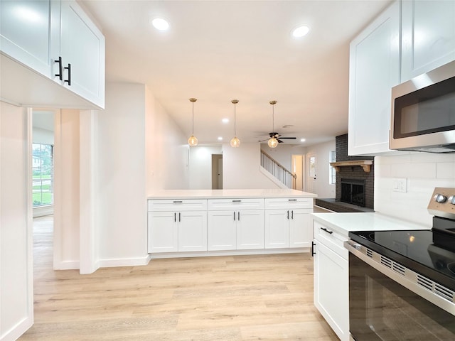 kitchen featuring light wood finished floors, decorative backsplash, a fireplace, a ceiling fan, and appliances with stainless steel finishes