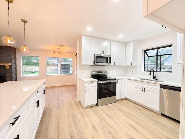 kitchen with decorative backsplash, a sink, appliances with stainless steel finishes, light wood-type flooring, and a fireplace