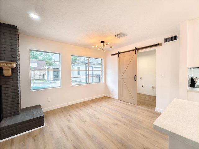 unfurnished living room with a barn door, light wood-style floors, visible vents, and a notable chandelier