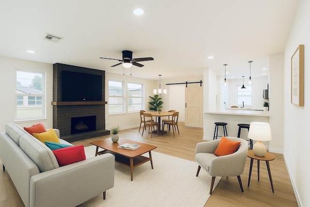 living room featuring a barn door, light wood-type flooring, visible vents, and baseboards