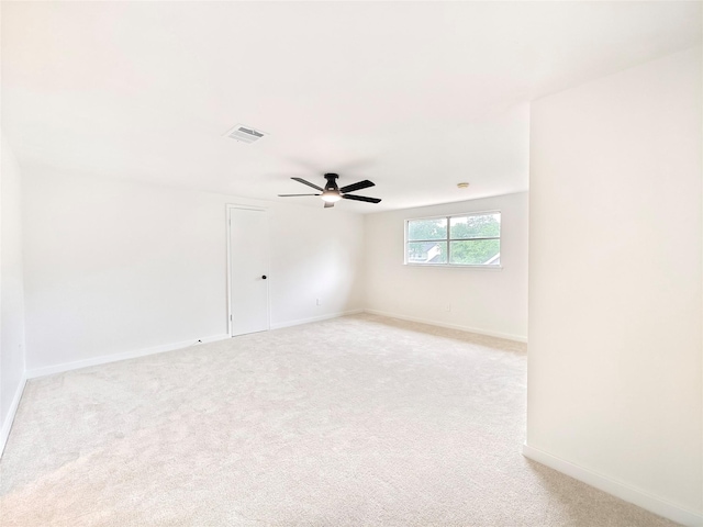 spare room with light colored carpet, visible vents, a ceiling fan, and baseboards