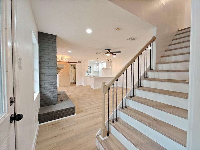 stairs with a barn door, a ceiling fan, visible vents, baseboards, and wood finished floors