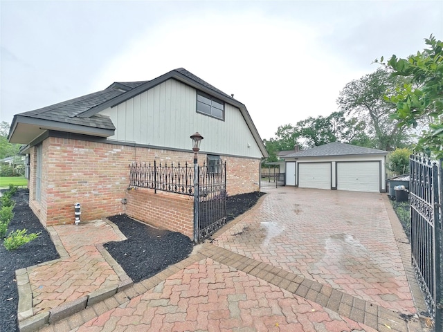 view of home's exterior with brick siding, fence, a shingled roof, an outbuilding, and a garage