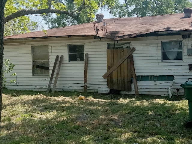 rear view of property with roof with shingles and a yard