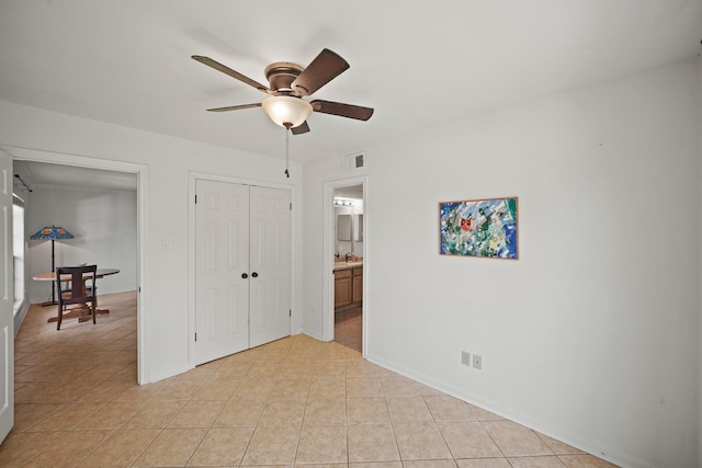 unfurnished bedroom featuring ensuite bath, baseboards, light tile patterned floors, visible vents, and a closet