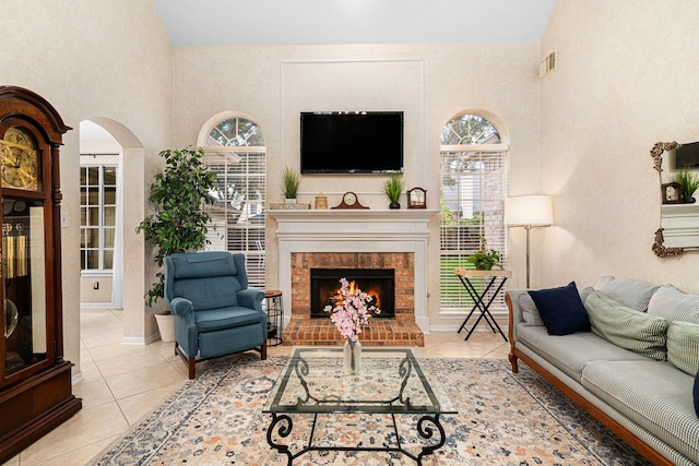 living room with tile patterned flooring, a fireplace, arched walkways, high vaulted ceiling, and visible vents