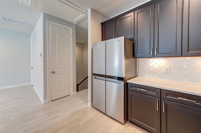 kitchen with light countertops, light wood-style flooring, freestanding refrigerator, tasteful backsplash, and visible vents
