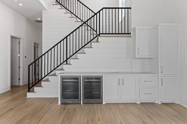11365 Beachside Dr, Galveston, TX 77554 - bar featuring wine cooler, light wood-type flooring, a towering ceiling, stairway, and baseboards