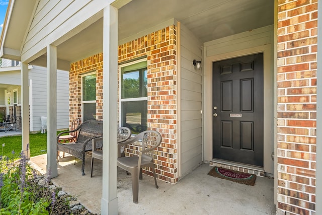 doorway to property featuring covered porch and brick siding
