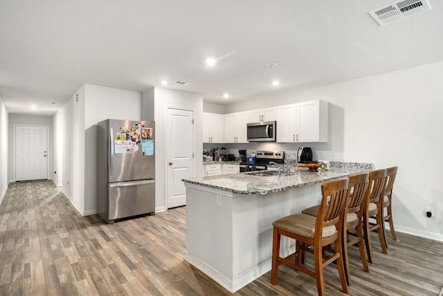 kitchen with appliances with stainless steel finishes, light stone counters, a sink, a peninsula, and visible vents