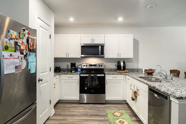 kitchen featuring light stone counters, appliances with stainless steel finishes, a sink, a peninsula, and wood finished floors