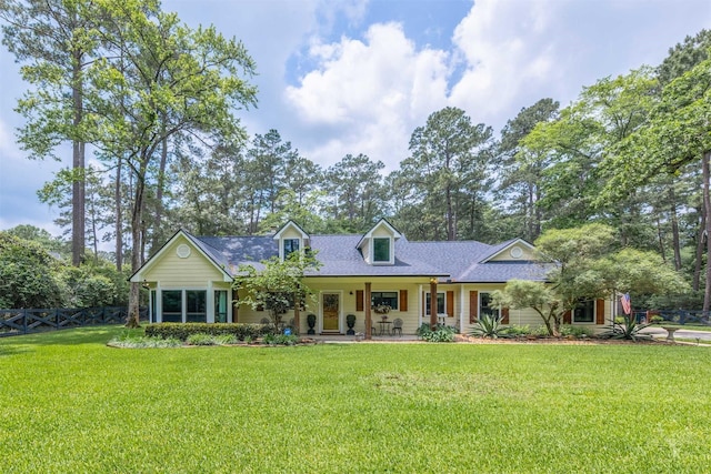 cape cod house with fence, roof with shingles, covered porch, and a front lawn