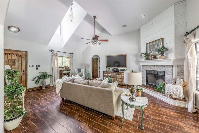 living room featuring a fireplace, high vaulted ceiling, a ceiling fan, baseboards, and dark wood-type flooring