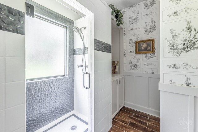 bathroom featuring wood tiled floor, a decorative wall, a stall shower, and a wainscoted wall