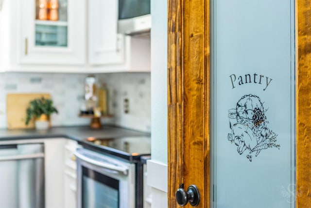 interior details featuring glass insert cabinets, range hood, electric stove, dishwashing machine, and white cabinetry