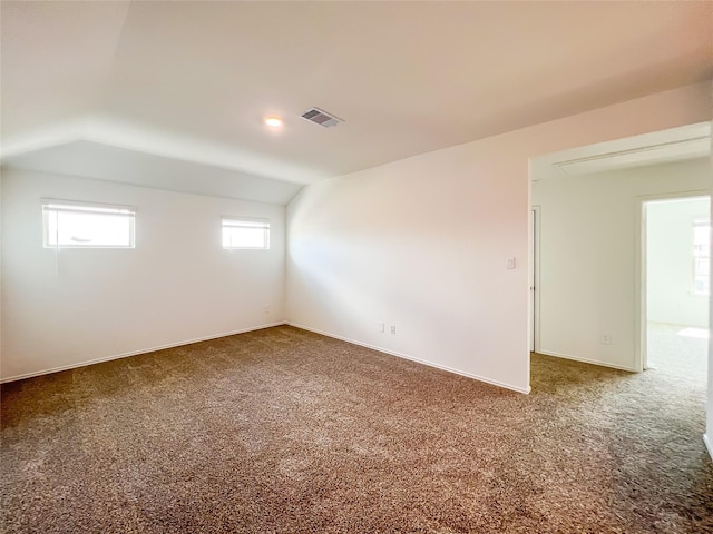 carpeted empty room with baseboards, lofted ceiling, and visible vents