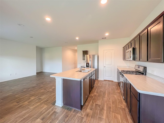 kitchen featuring a kitchen island with sink, light wood-style floors, light countertops, a sink, and appliances with stainless steel finishes