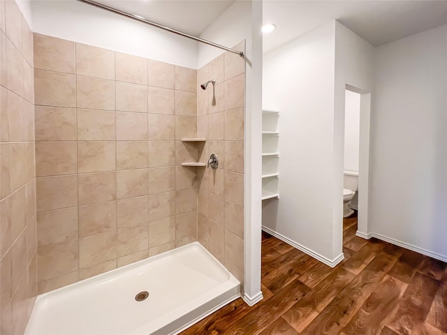 bathroom featuring toilet, tiled shower, and wood finished floors