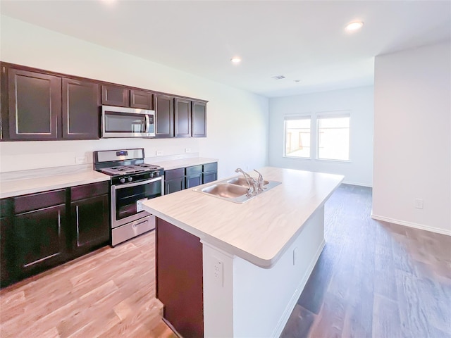 kitchen featuring dark brown cabinetry, light countertops, a sink, light wood finished floors, and stainless steel appliances