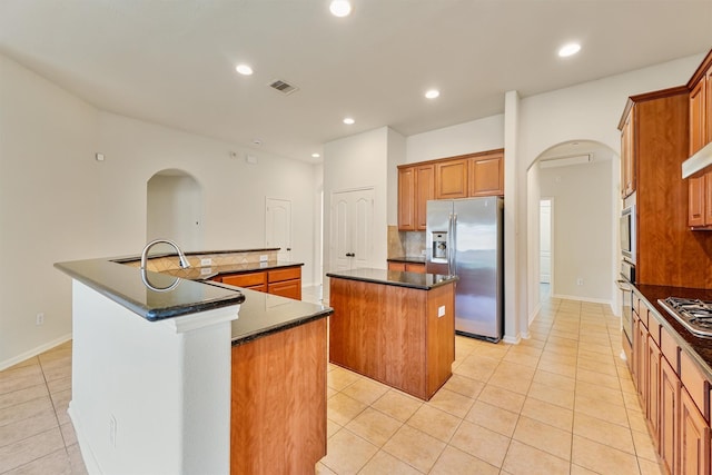 kitchen with light tile patterned flooring, recessed lighting, a large island with sink, arched walkways, and stainless steel appliances