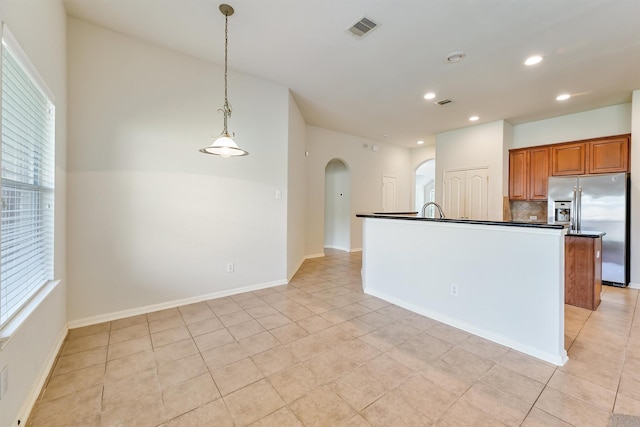 kitchen with brown cabinets, dark countertops, arched walkways, stainless steel refrigerator with ice dispenser, and visible vents