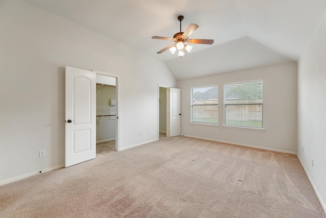 unfurnished bedroom with baseboards, light carpet, a walk in closet, and lofted ceiling