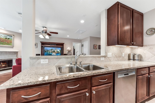 kitchen with ceiling fan, tasteful backsplash, stainless steel dishwasher, a sink, and a glass covered fireplace