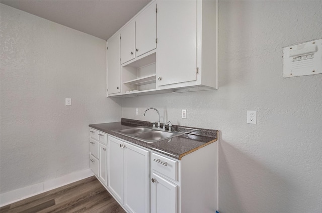 kitchen with dark countertops, a sink, baseboards, dark wood-style floors, and white cabinetry
