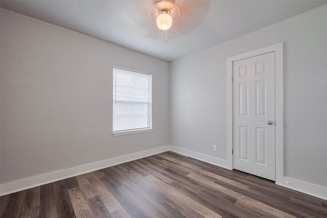 empty room featuring baseboards, ceiling fan, and dark wood-type flooring