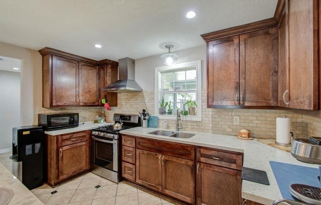 kitchen with stainless steel gas range, black microwave, a sink, wall chimney exhaust hood, and tasteful backsplash