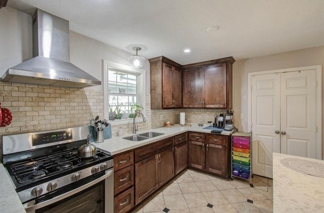 kitchen with wall chimney range hood, gas stove, light countertops, a sink, and light tile patterned flooring