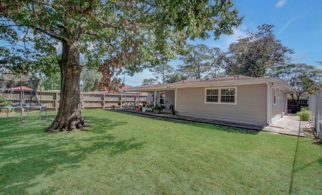 rear view of house featuring a yard, a fenced backyard, and a trampoline