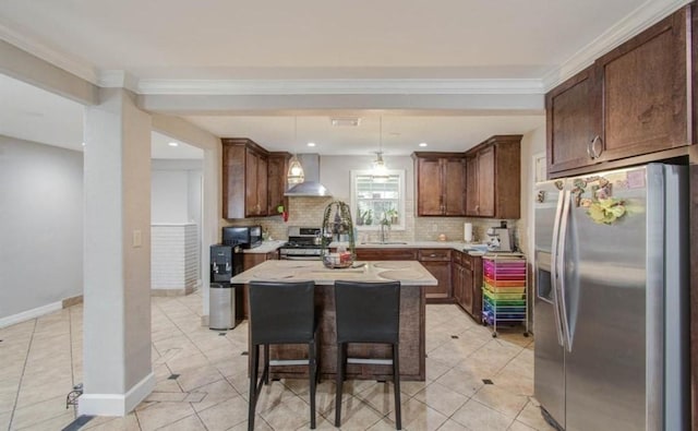kitchen featuring wall chimney range hood, light countertops, stainless steel appliances, decorative backsplash, and a kitchen island