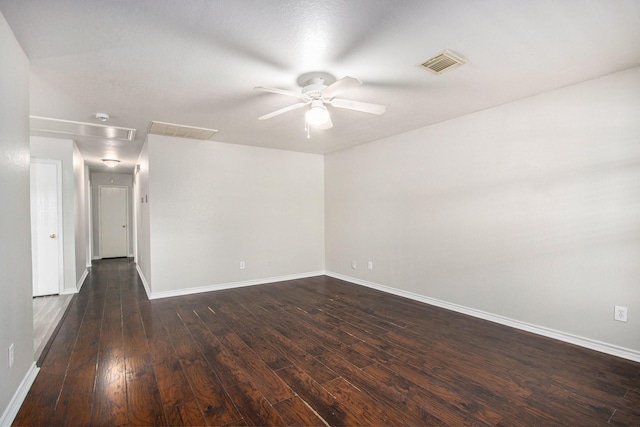 empty room featuring visible vents, baseboards, attic access, a ceiling fan, and dark wood finished floors