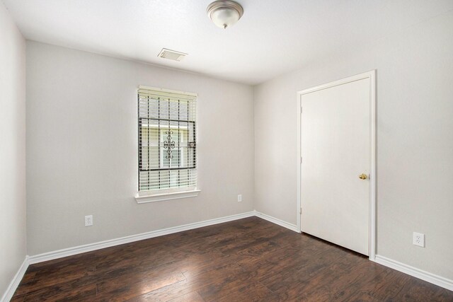 unfurnished room featuring baseboards, dark wood-style floors, and visible vents