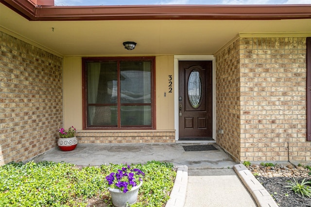 view of exterior entry with brick siding and covered porch
