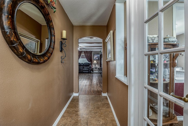 hall featuring a textured ceiling, baseboards, and a textured wall