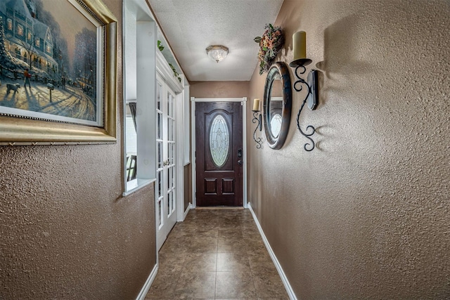 entryway with baseboards, a textured wall, french doors, and a textured ceiling