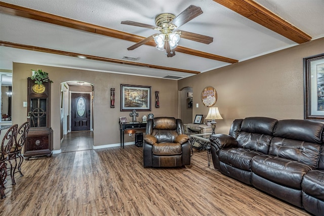 living room with ceiling fan, arched walkways, wood finished floors, beamed ceiling, and visible vents
