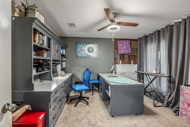 home office with visible vents, a textured wall, ceiling fan, light colored carpet, and a textured ceiling