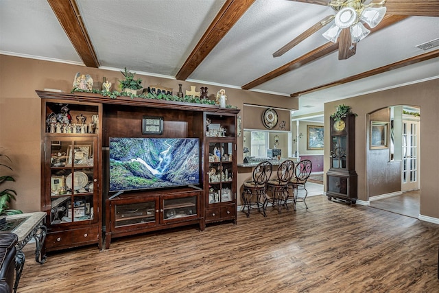 living area featuring arched walkways, beamed ceiling, visible vents, and wood finished floors
